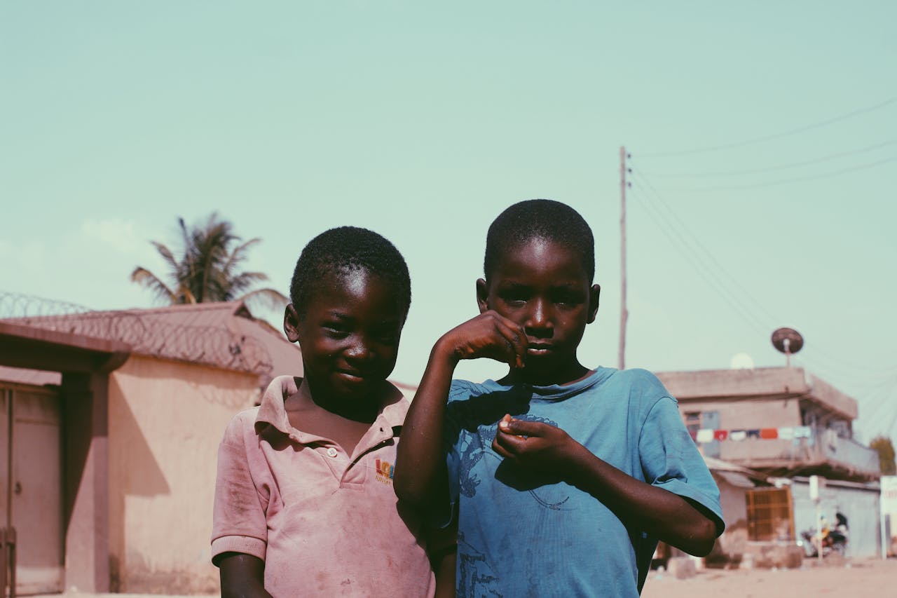 services-03 Two African boys smiling and posing outdoors, showcasing friendship in a rural setting.